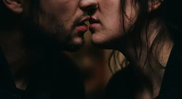 A close-up of two people about to kiss, featuring only their subtle expressions and dim lighting, creating an intimate and romantic atmosphere