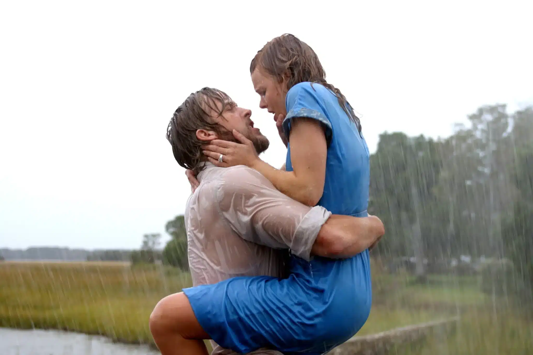 A couple, soaking wet in the rain, embraces passionately outdoors with a blurred background of greenery