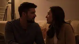 A happy young couple hugging on a sofa indoors with a lit fireplace and soft string lights in the background
