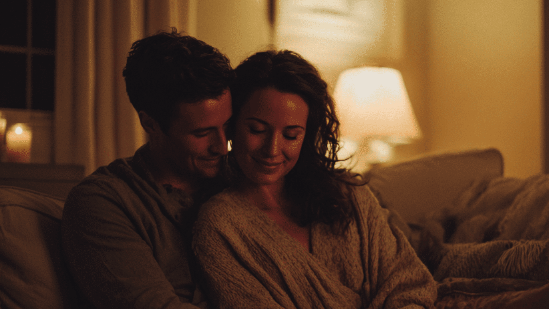A man and woman sit on a floor in warm candle light laughing while holding a book during a cozy indoor date night at home