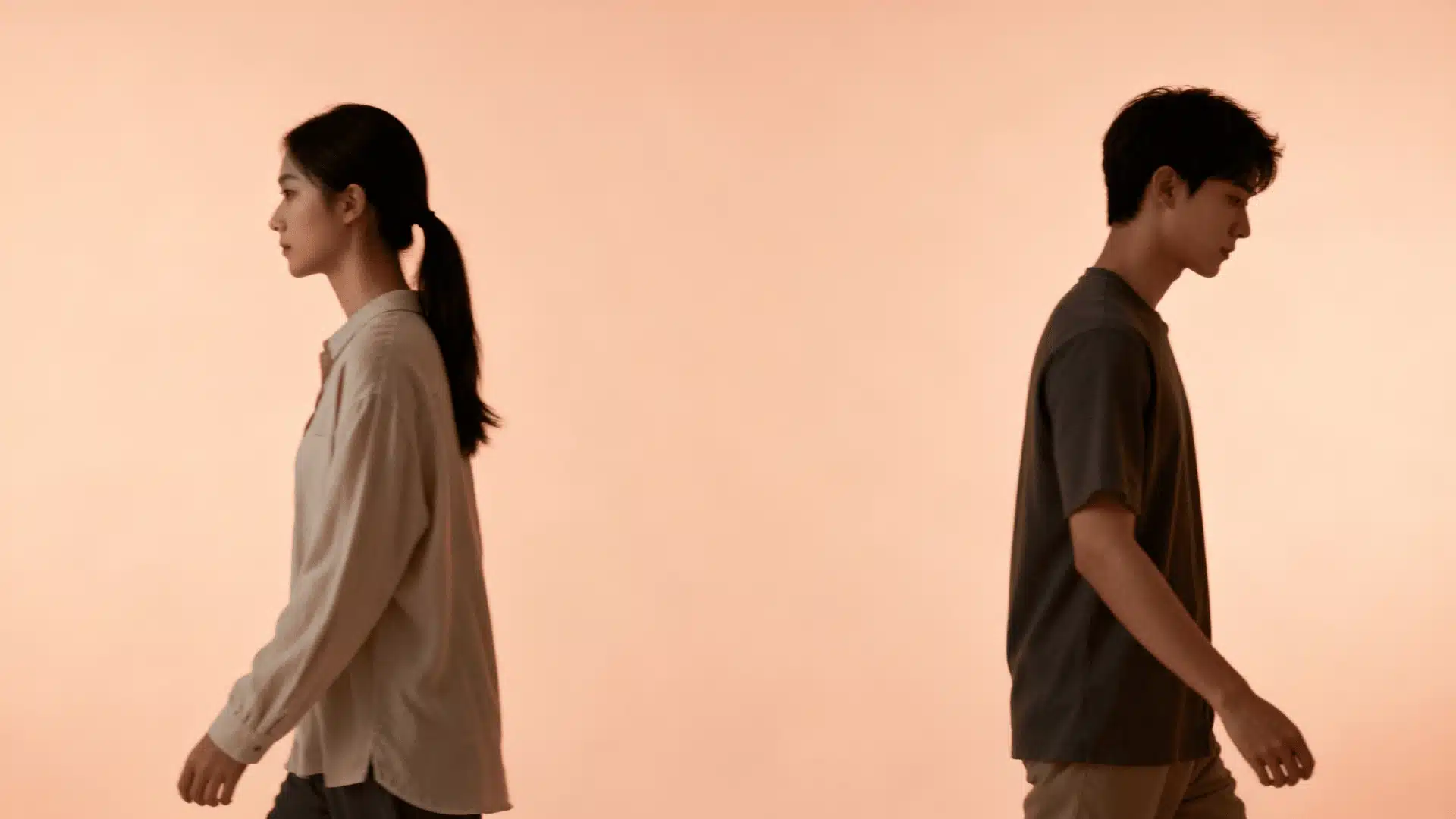 A man and woman walk away from each other in opposite directions against a soft neutral background