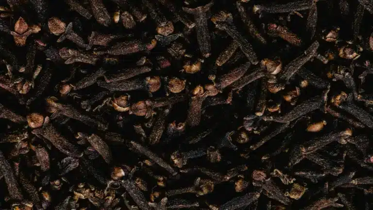 A tightly packed, close-up image of dark brown, whole dried cloves