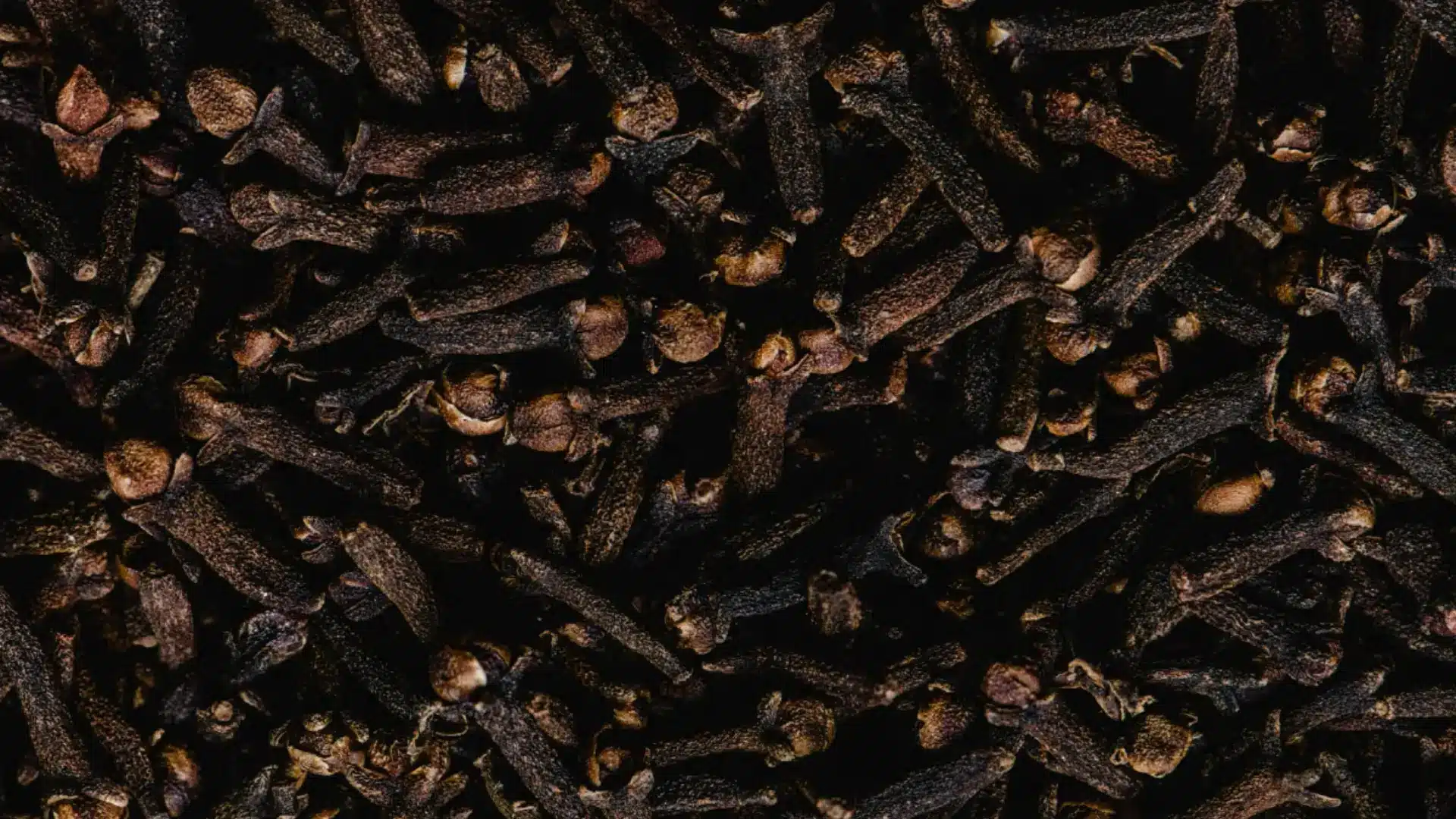 A tightly packed, close-up image of dark brown, whole dried cloves
