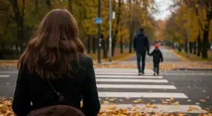 A woman with long brown hair stands facing away while a man and his child cross a zebra crossing