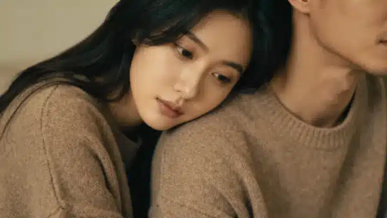 A woman with long dark hair leans her head gently on a man's shoulder, both wearing cozy beige sweaters
