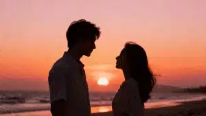 Couple silhouettes facing each other on a beach at sunset with warm orange sky and ocean waves in background