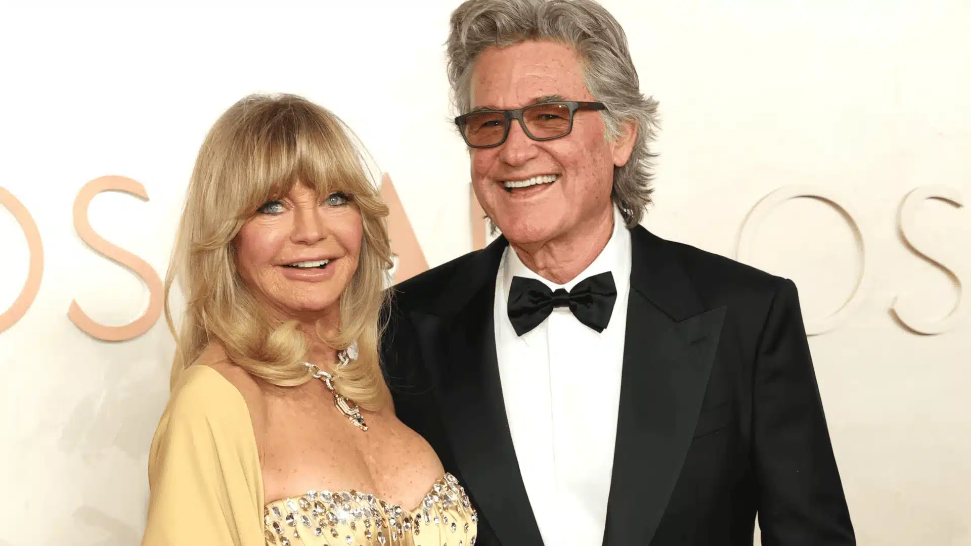 Goldie Hawn and Kurt Russell smiling together on the red carpet, dressed in elegant evening attire at a formal awards event
