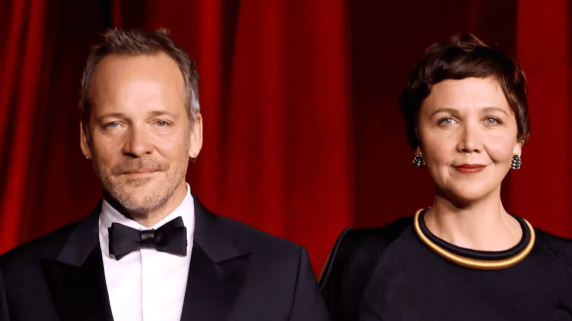Maggie Gyllenhaal and Peter Sarsgaard posing together in formal attire in front of a red curtain backdrop at an awards event