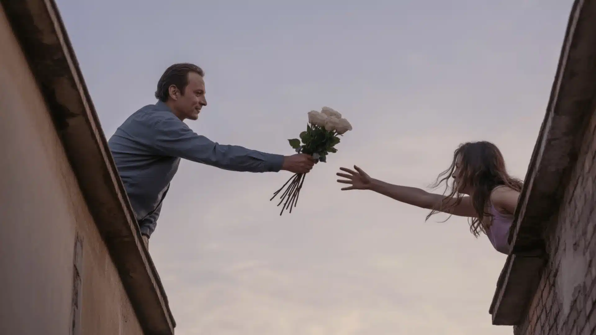 Man offering flowers to woman across balconies reaching out in a romantic moment