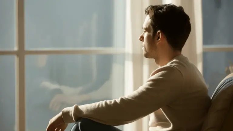 Man sitting by window in warm sunlight, looking outside, calm mood, side profile, soft indoor setting