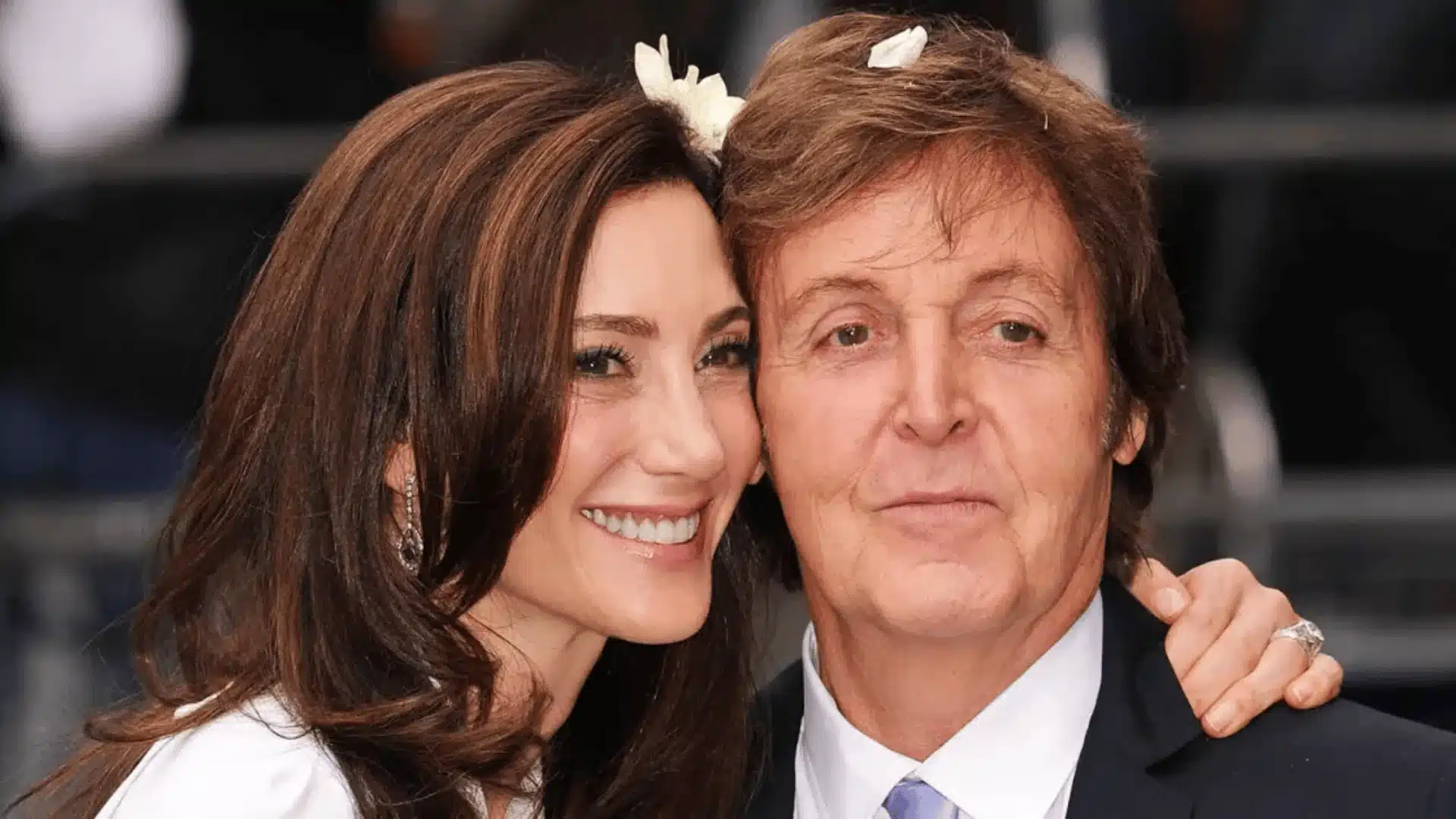 Paul McCartney and Nancy Shevell pose together at an event, both smiling and showing a friendly, warm demeanor
