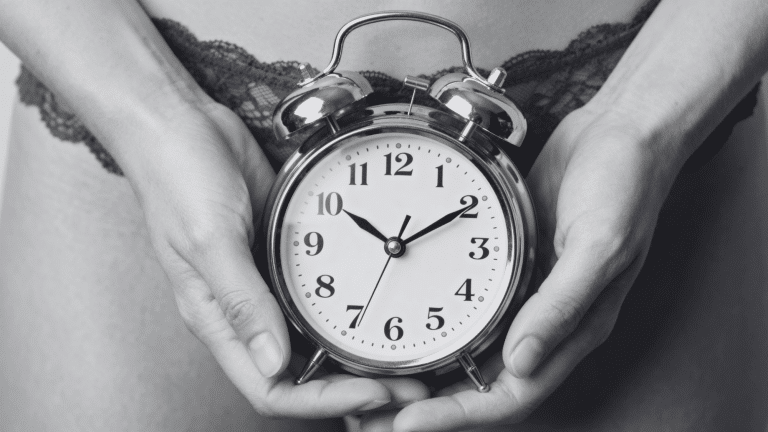 Person holding a silver analog alarm clock over the lower torso representing delayed periods.