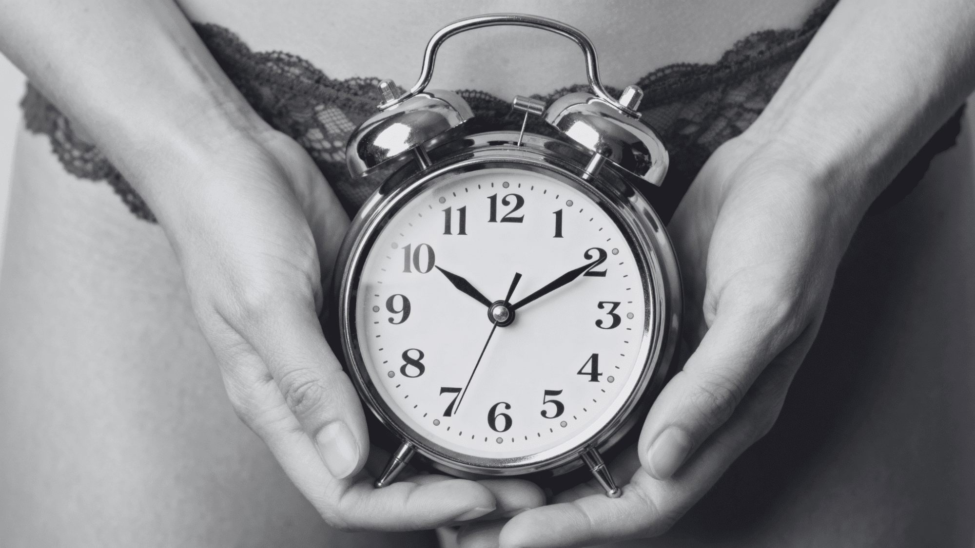 Person holding a silver analog alarm clock over the lower torso representing delayed periods.
