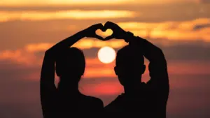 Silhouette of couple forming heart with hands against sunset sky over ocea
