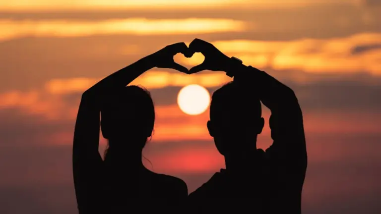 Silhouette of couple forming heart with hands against sunset sky over ocea