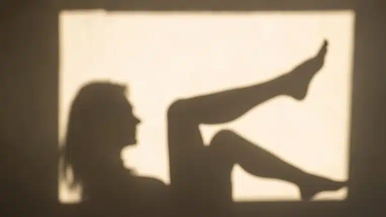 Silhouette shadow of a woman reclining with her legs raised against a brightly lit rectangular background