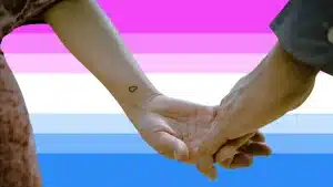 Two women hold hands against a bi-curious flag in the background