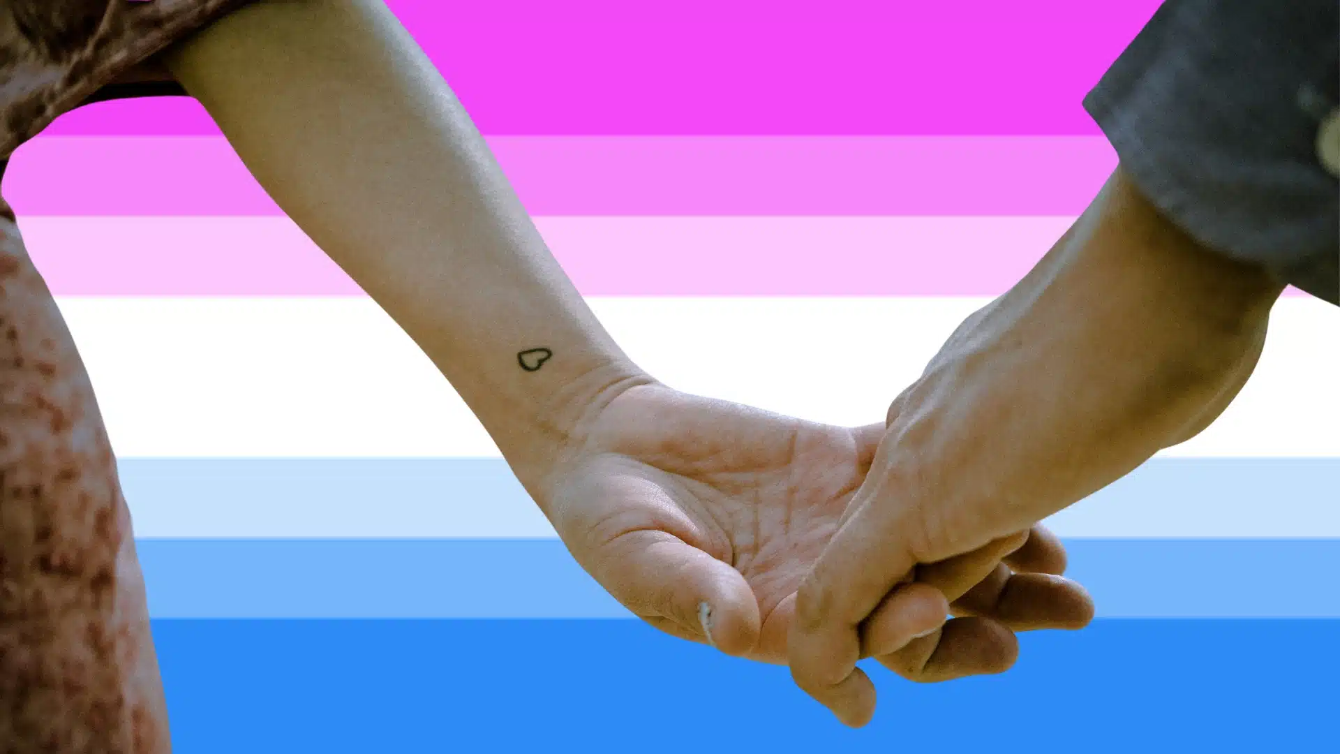 Two women hold hands against a bi-curious flag in the background