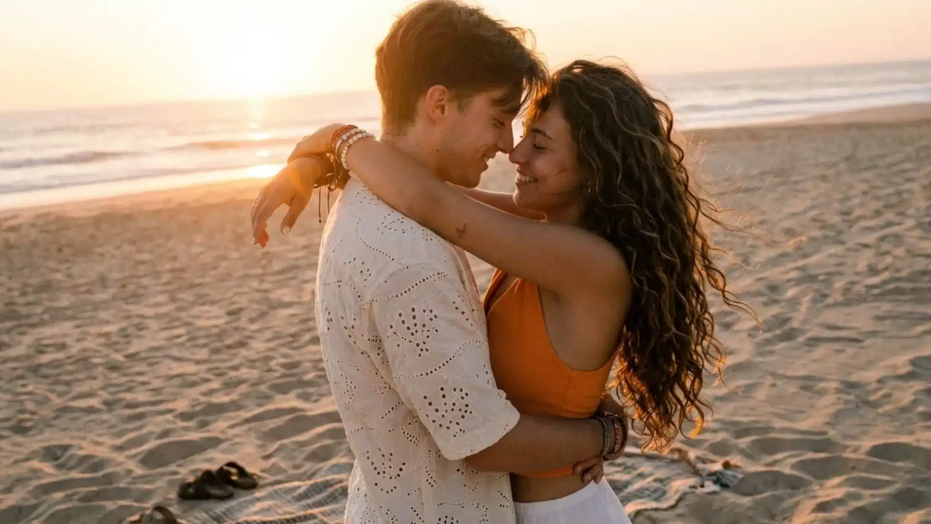 a man and woman hug on a sandy beach during sunset as they look at each other with big smiles in a warm outdoor setting