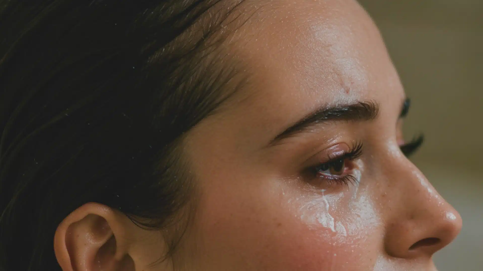 A close-up of a woman’s face showing dark hair, sweating skin, and a tear rolling down her cheek