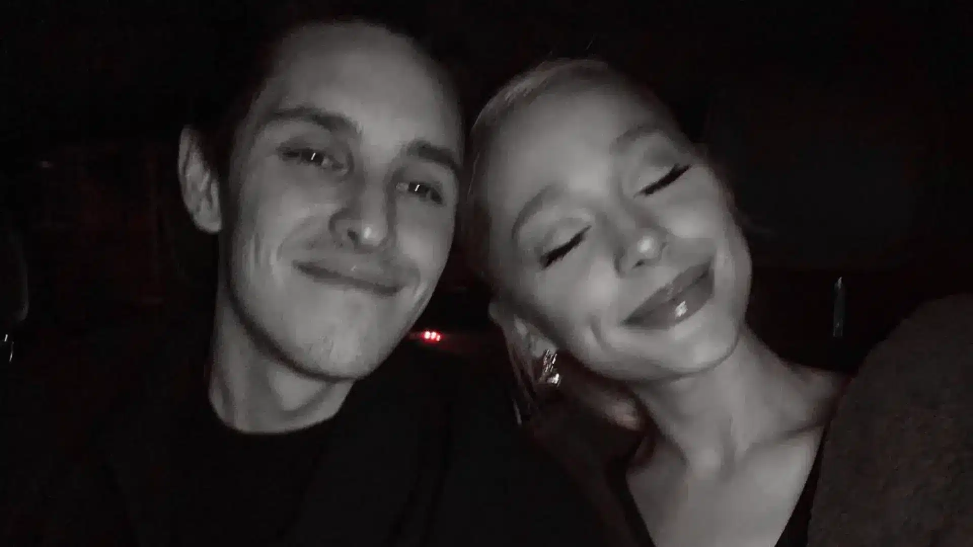 Black and white close-up selfie of Dalton Gomez and Ariana Grande with closed eyes leaning close together in a dark setting.