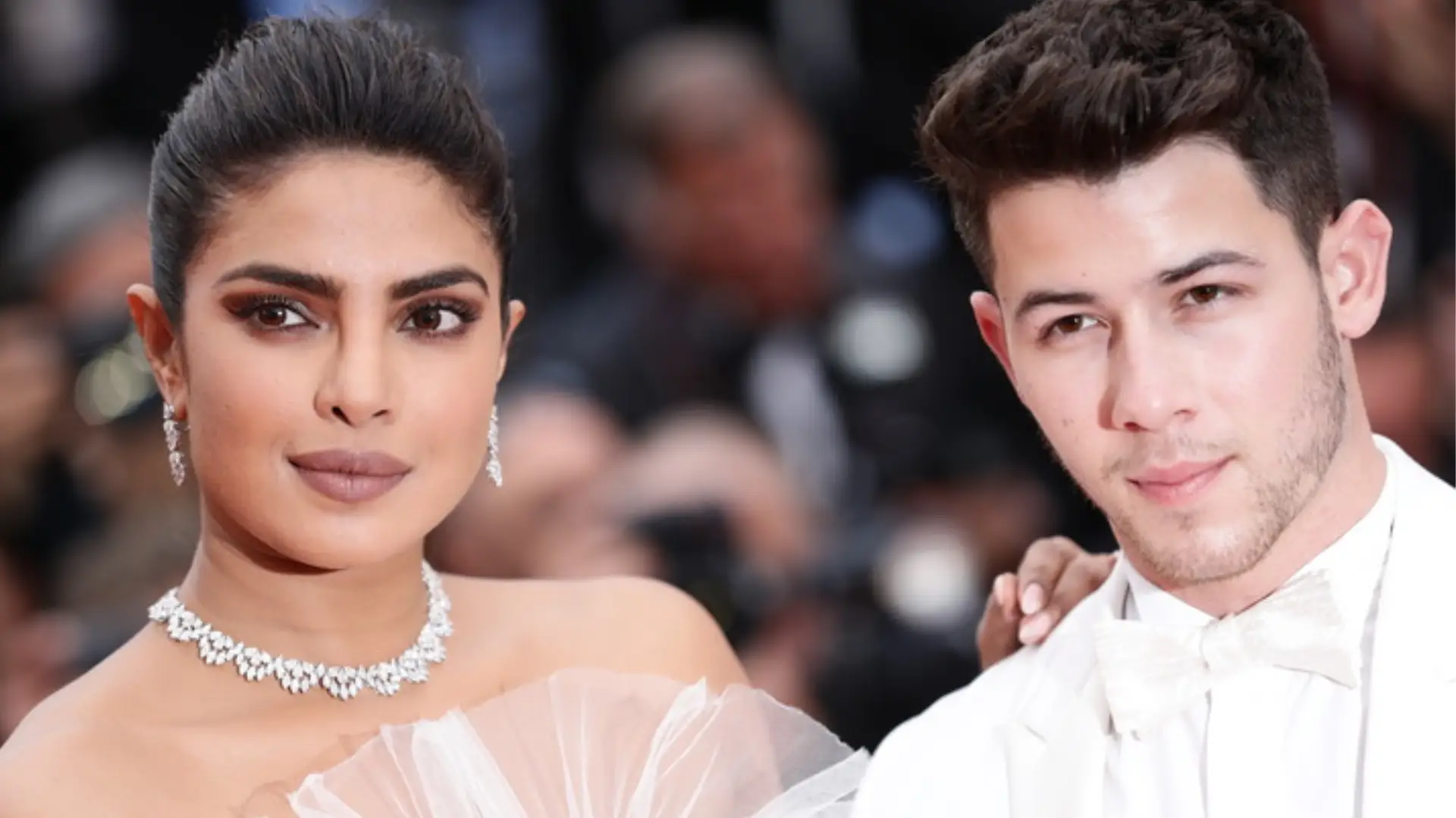 Priyanka Chopra and Nick Jonas pose together on a red carpet, with Chopra wearing a diamond necklace and Jonas in a white tuxedo