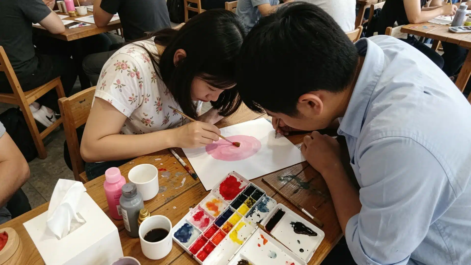 Two people are actively painting on a table, with paintbrushes and vibrant colors scattered around them.