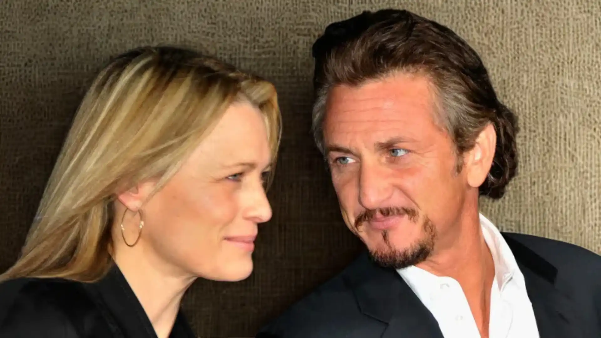 Robin Wright and Sean Penn look toward each other in a close-up portrait against a textured, dark background.