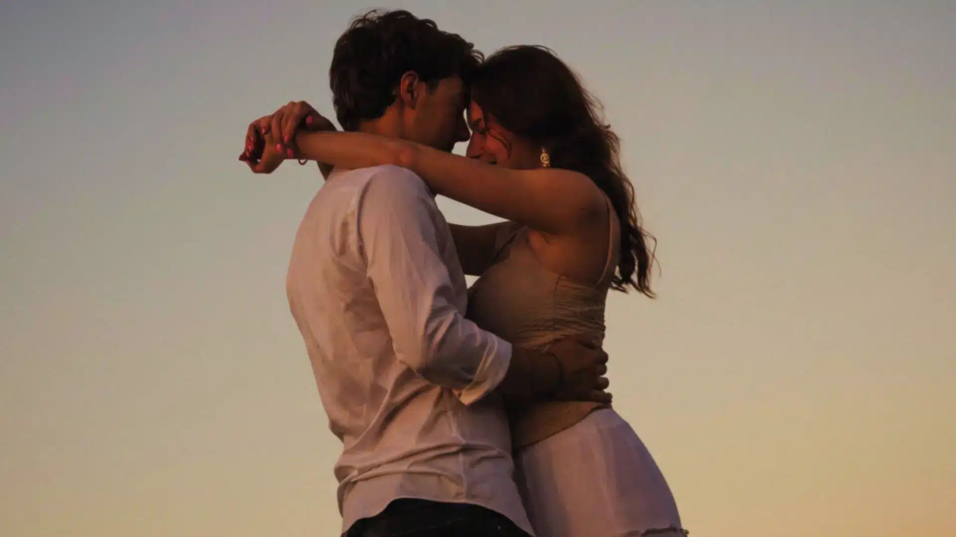 A man and woman embrace in a tender hug outdoors at dusk with their heads touching in a soft and romantic silhouette
