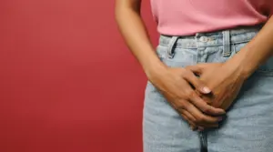 A woman stands with her hands resting on her stomach, conveying a sense of contemplation or discomfort.