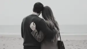 A couple embracing on a sandy beach with the ocean in the background.