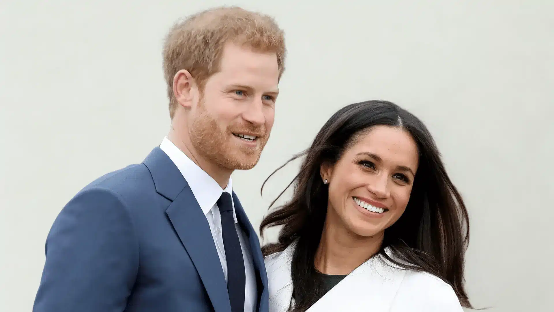 Prince Harry and Meghan Markle smile at the camera in formal attire.