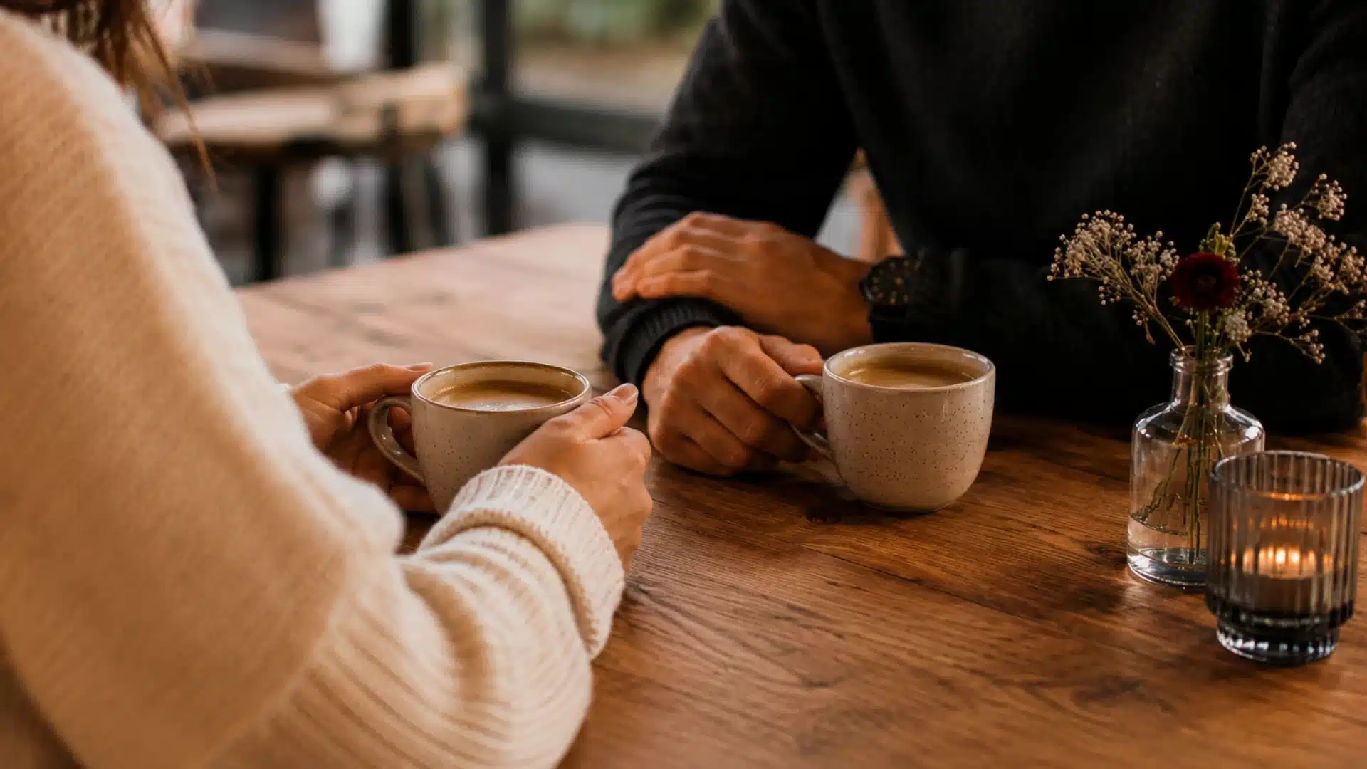 couple enjoying a date over matching coffee mugs in a cozy cafe with faces out of frame warm natural atmosphere