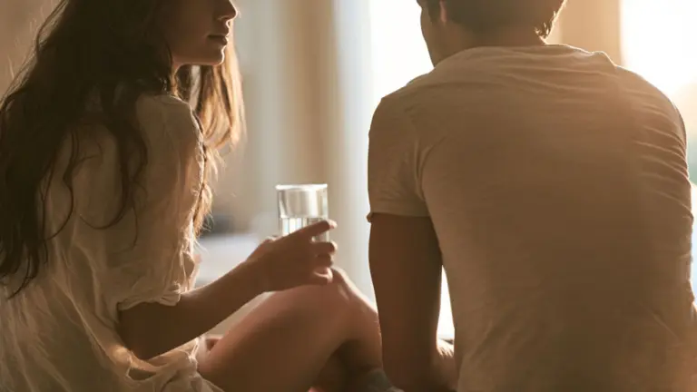 Couple sitting together in warm sunlight near a window with the woman holding a glass of water