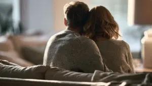 Couple sitting closely together on a sofa viewed from behind in a warmly lit living room
