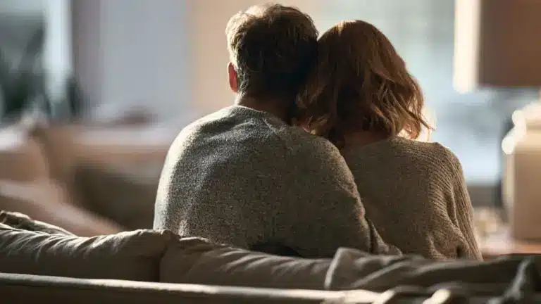 Couple sitting closely together on a sofa viewed from behind in a warmly lit living room